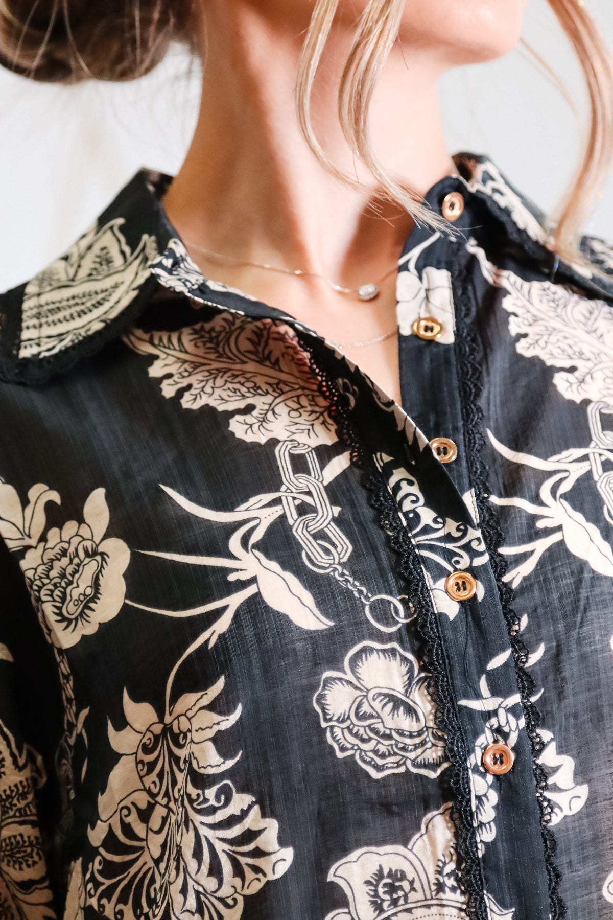 Close-up of a person wearing a black floral patterned shirt with gold buttons.