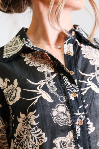 Close-up of a person wearing a black floral patterned shirt with gold buttons.
